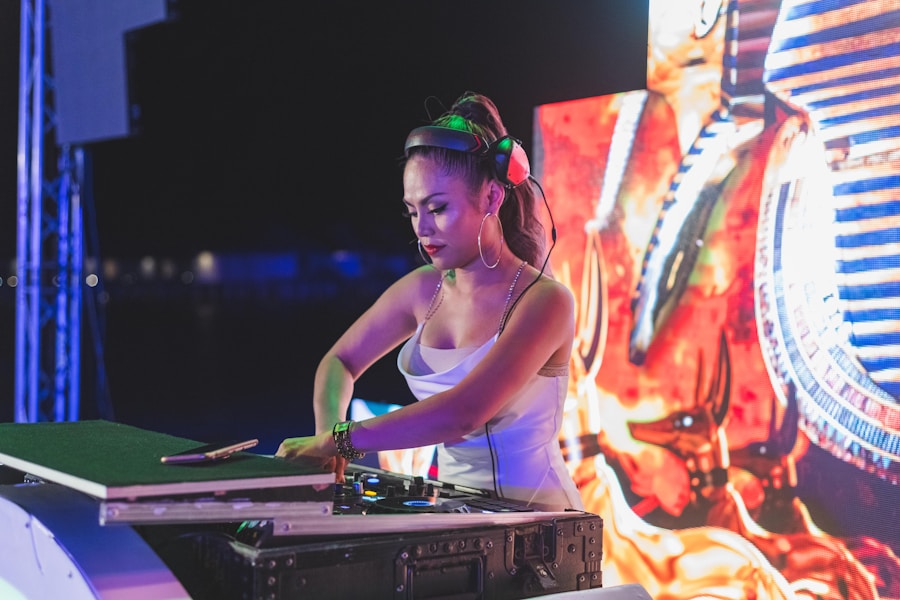 Una DJ con auriculares y traje blanco mezcla música en una consola de DJ en un animado evento, con luces de colores y una gran pantalla digital de fondo.