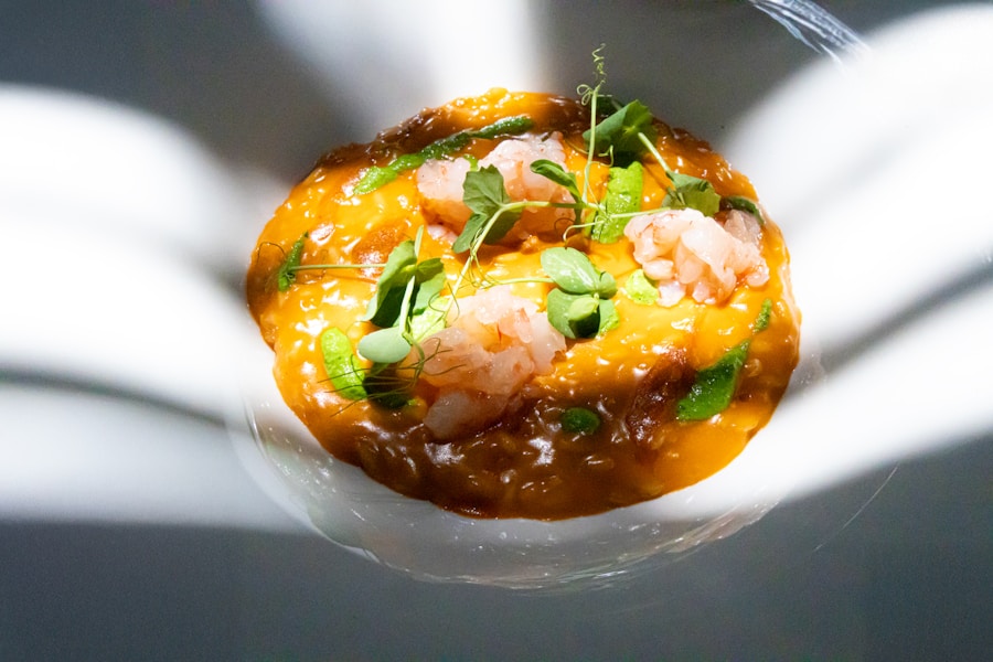 Un primer plano de un risotto gourmet, de un intenso color anaranjado, adornado con trozos de gambas crudas y microgreens verdes, presentado en un plato blanco bajo una espectacular luz difusa.