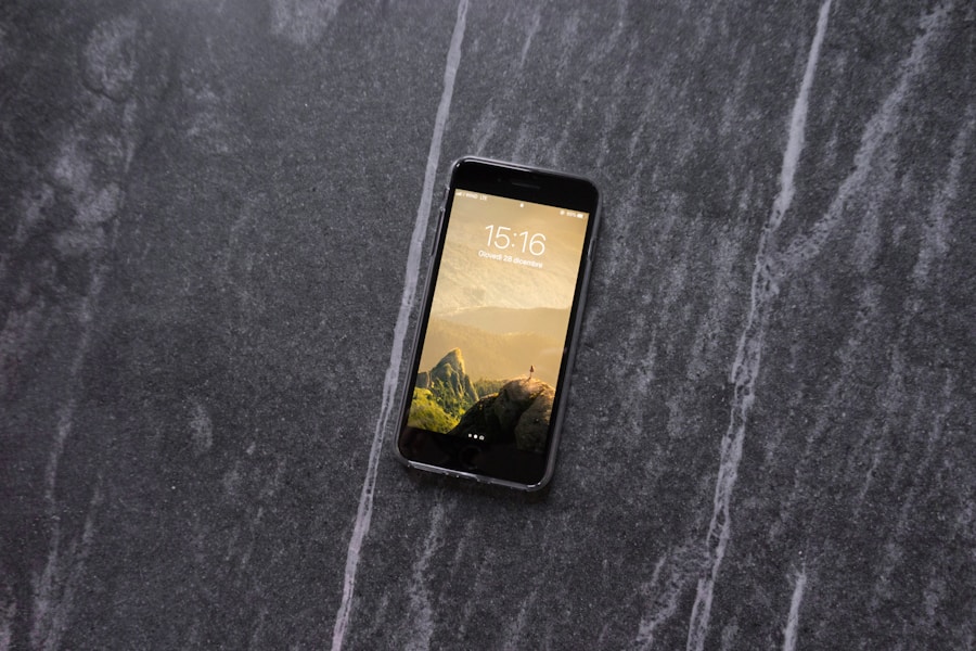 Un smartphone con pantalla de bloqueo de paisaje montañoso muestra la hora 15:16, apoyado sobre una superficie de mármol gris oscuro con vetas claras.