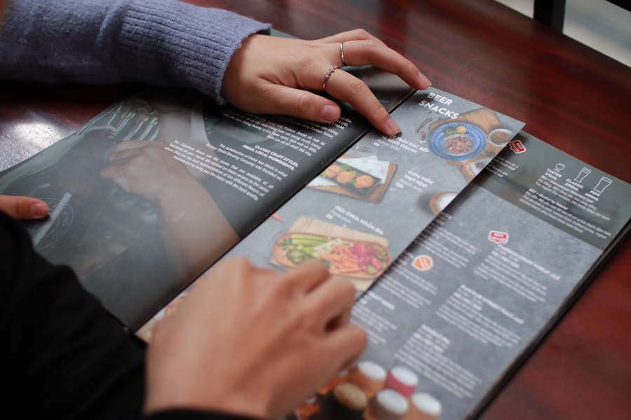 Dos personas se sientan en una mesa y miran un menú con fotos y descripciones de comidas y bebidas. Una persona señala un plato mientras la otra mantiene abierta la carta.